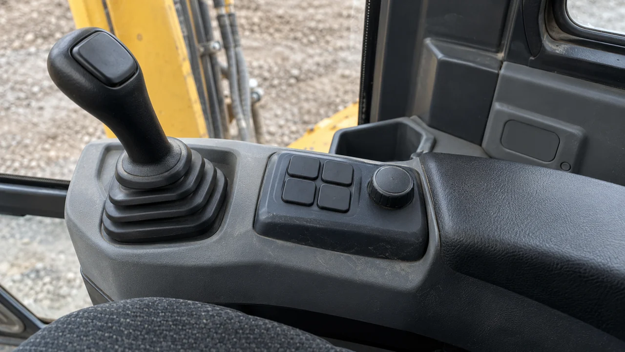 Black keypad buttons, a round dial and a joystick on a gray excavator armrest.